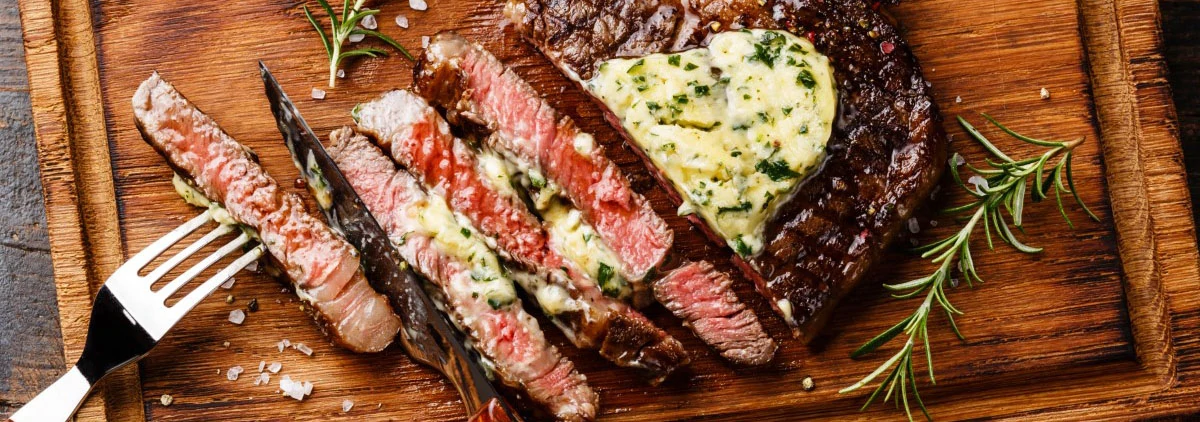 Sliced steak with herbs and butter on top on wood cutting board
