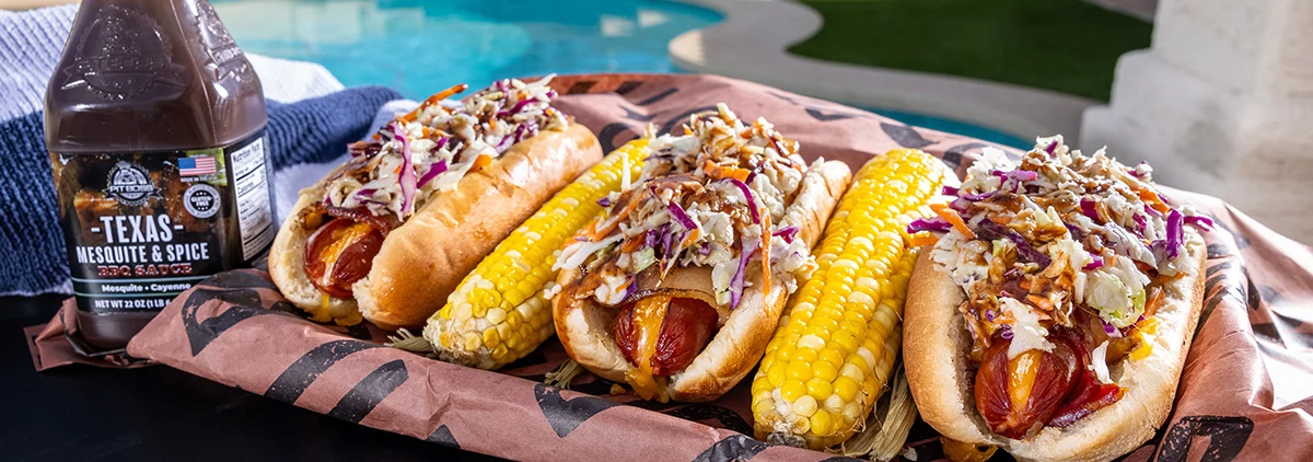 Hot dogs with corn next to a Pit Boss Texas Mesquite and Spice Sauce Bottle served on pit boss butcher paper