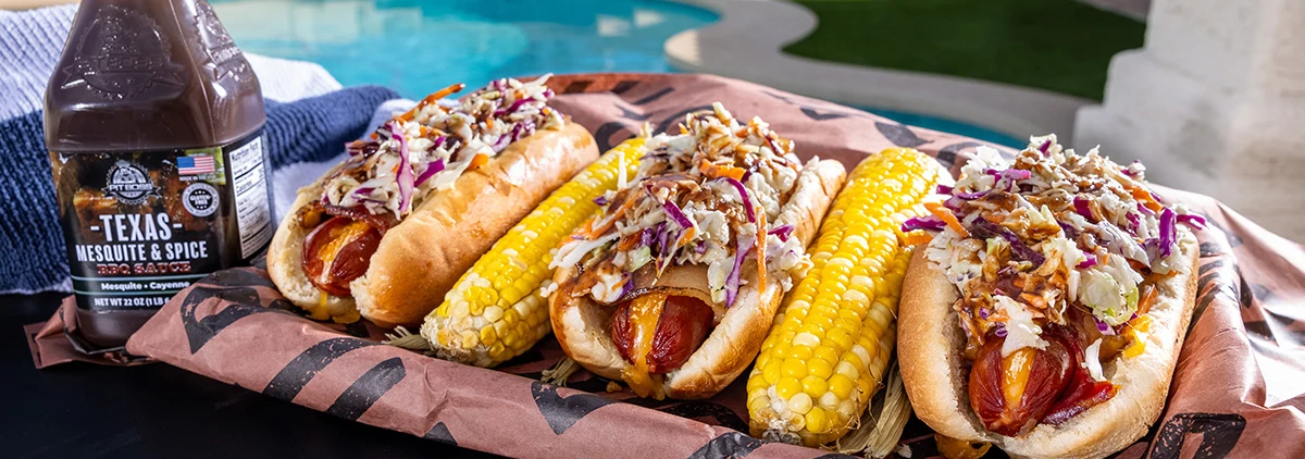 Hot dogs with corn, next to a Pit Boss Texas Mesquite and Spice Sauce Bottle