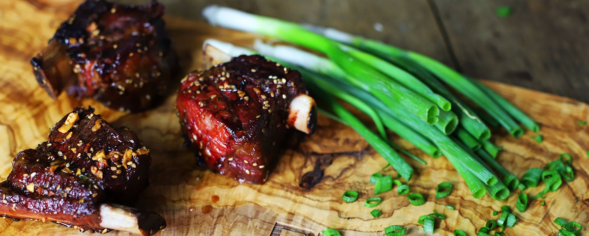 korean short ribs with sesame seeds next to green onions on a wood cutting board