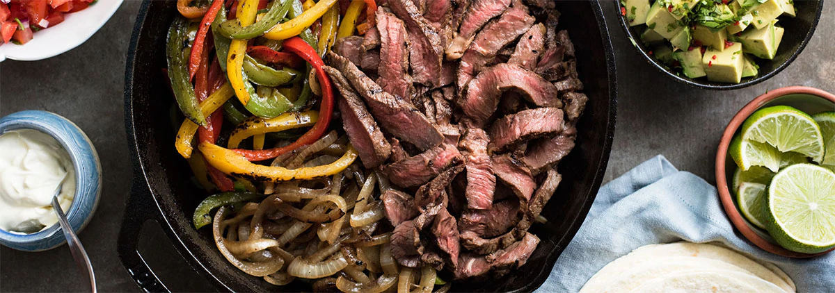 Cast Iron skillet with fajitas next to lime, avocado and sour cream