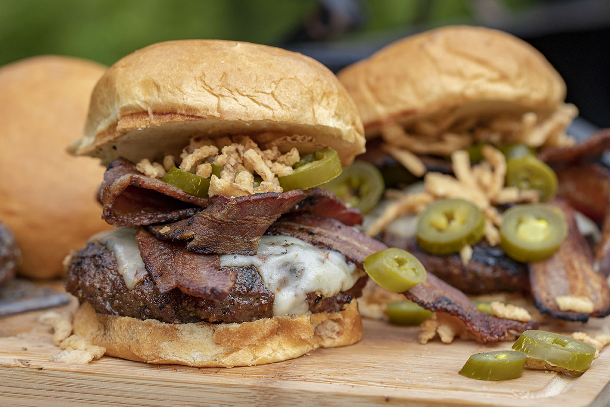 Burgers with onions and bacon next to a bottle of hickory bacon rub