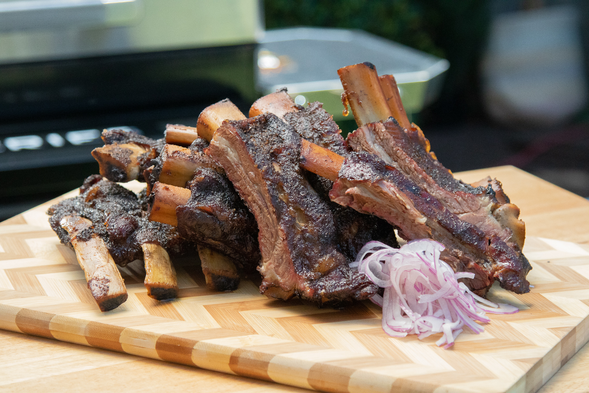 Sliced smoked beef ribs on wooden cutting board in front of Pit Boss Pro Series Elite Wood Pellet Grill