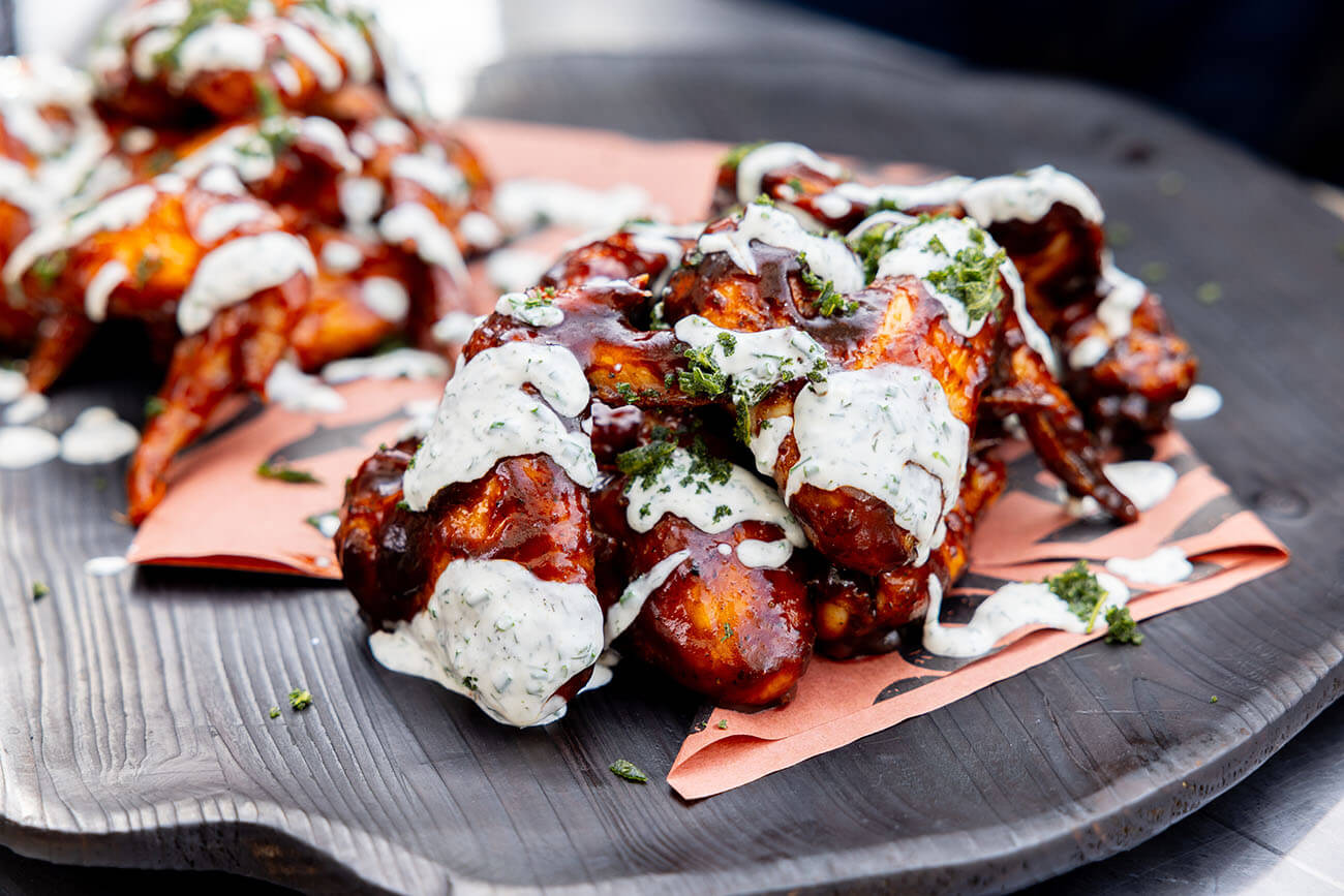 bbq grilled and smoked chicken wings crispy skin with homemade ranch drizzle on black plate