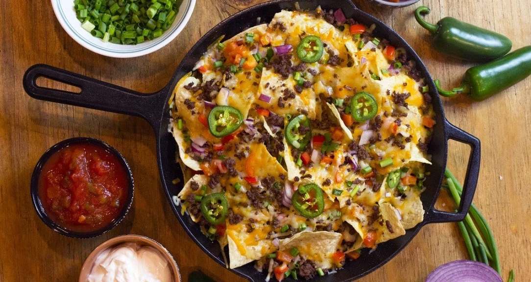 Cast Iron nachos next to salsa and jalapeno on top