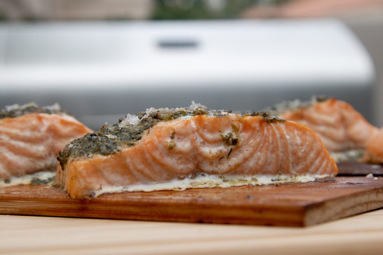 slice of salmon with butter and salt on top of wooden cutting board in front of Pit Boss Grill