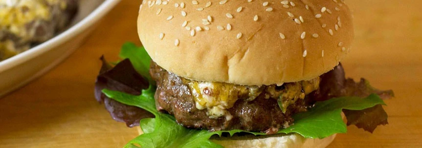 delicious looking Cheddar Stuffed burger with bun and lettuce on table