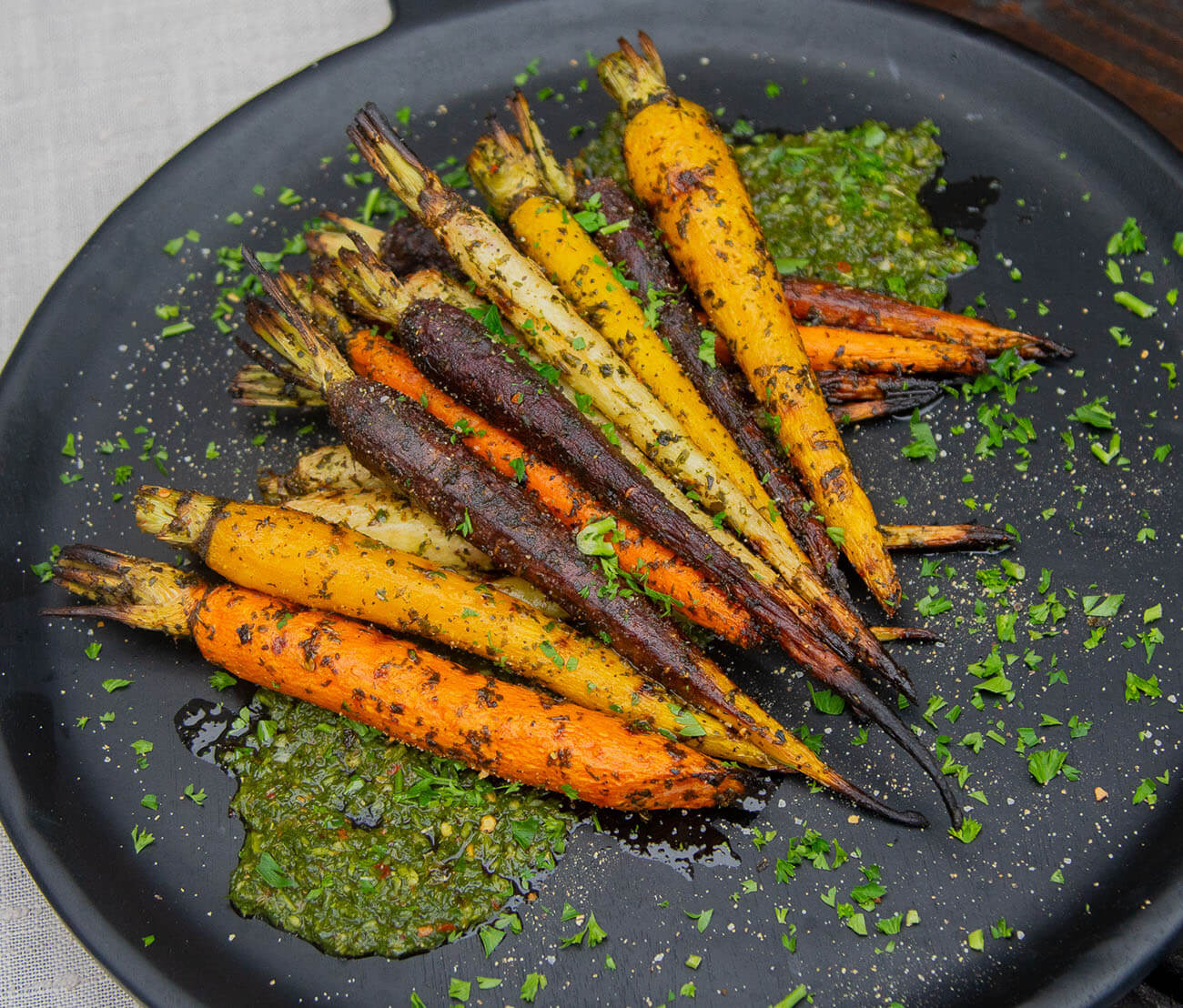 Roasted rainbow carrots on a plate with a green chimichurri, herb sauce