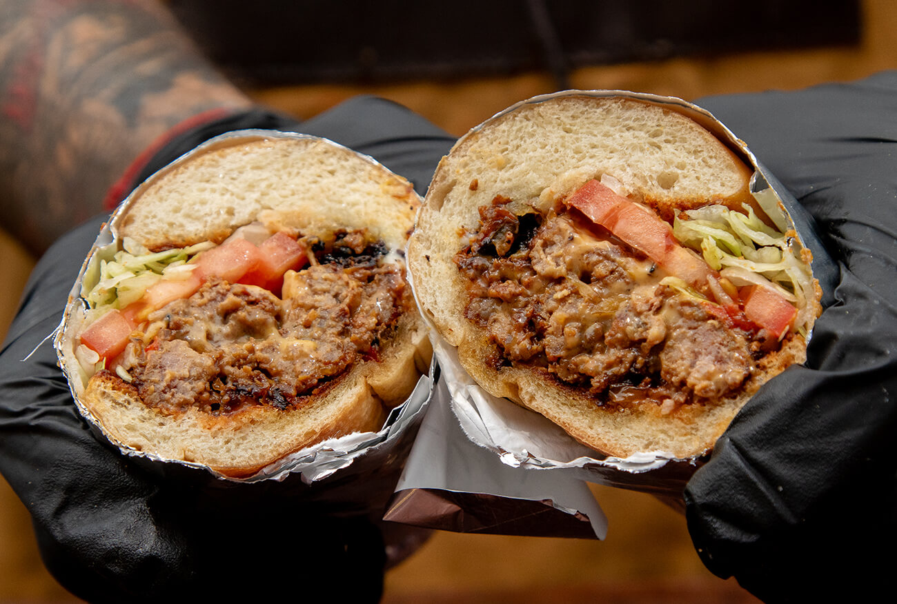 Chopped cheese sandwich cut in half wrapped in foil on a hero roll bun.