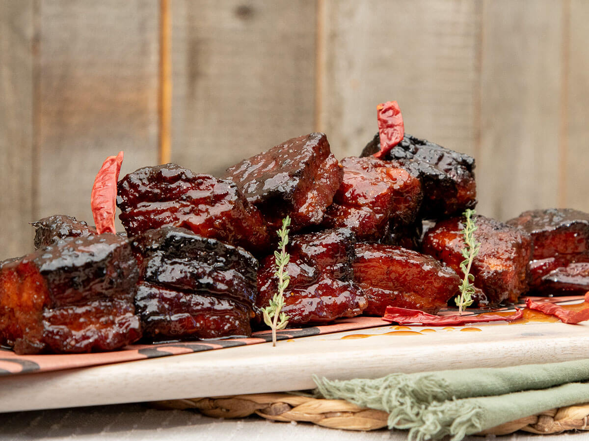 smoked and braised apple cider pork belly burnt ends cooked on a pit boss wood pellet grill plated with peppers and herbs