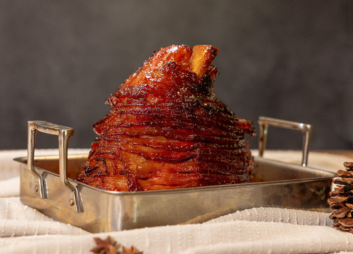 smoked spiral cut ham with homemade apple cider mustard glaze cooked on pit boss wood pellet grill served in metal roasting pan on holiday table