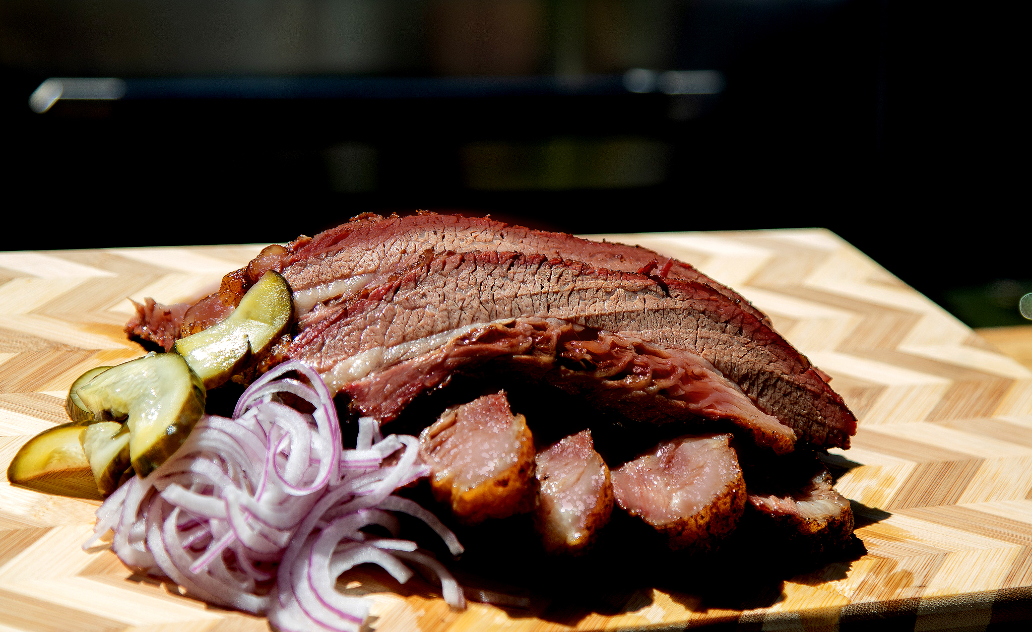 sliced smoke brisket cooked on pit boss hardwood pellet grill on wooden cutting board with pickled onions and pickles as garnish