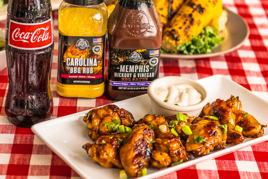 wings with sauce and garnish on white plate in front of pit boss spices and bottle of coca cola