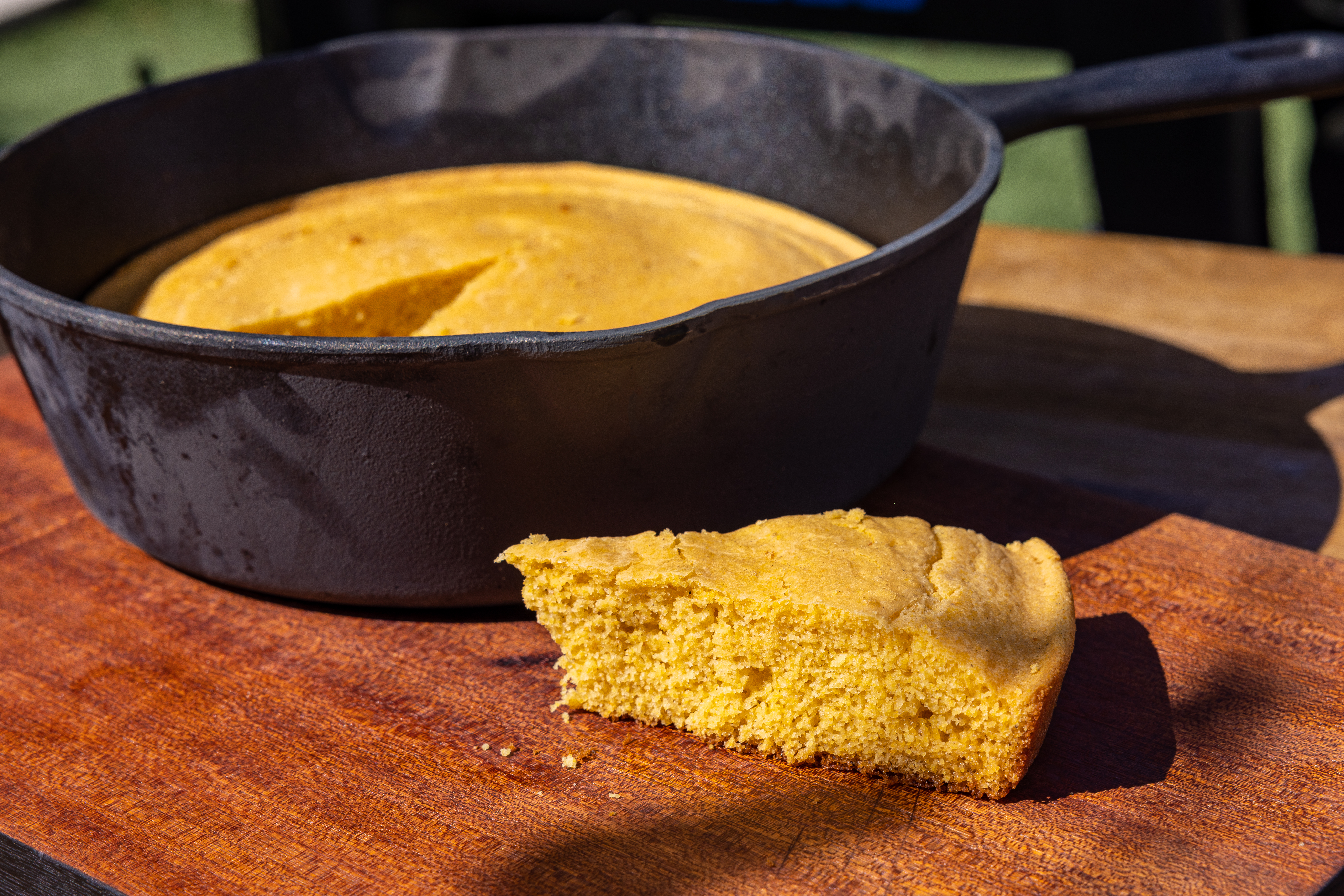 Up close of slice of cornbread, while rest of it is in a deep cast iron skillet in background