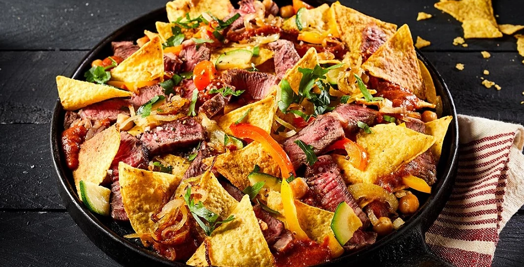 Nachos on a black plate with Rib eye, zucchini and bell peppers