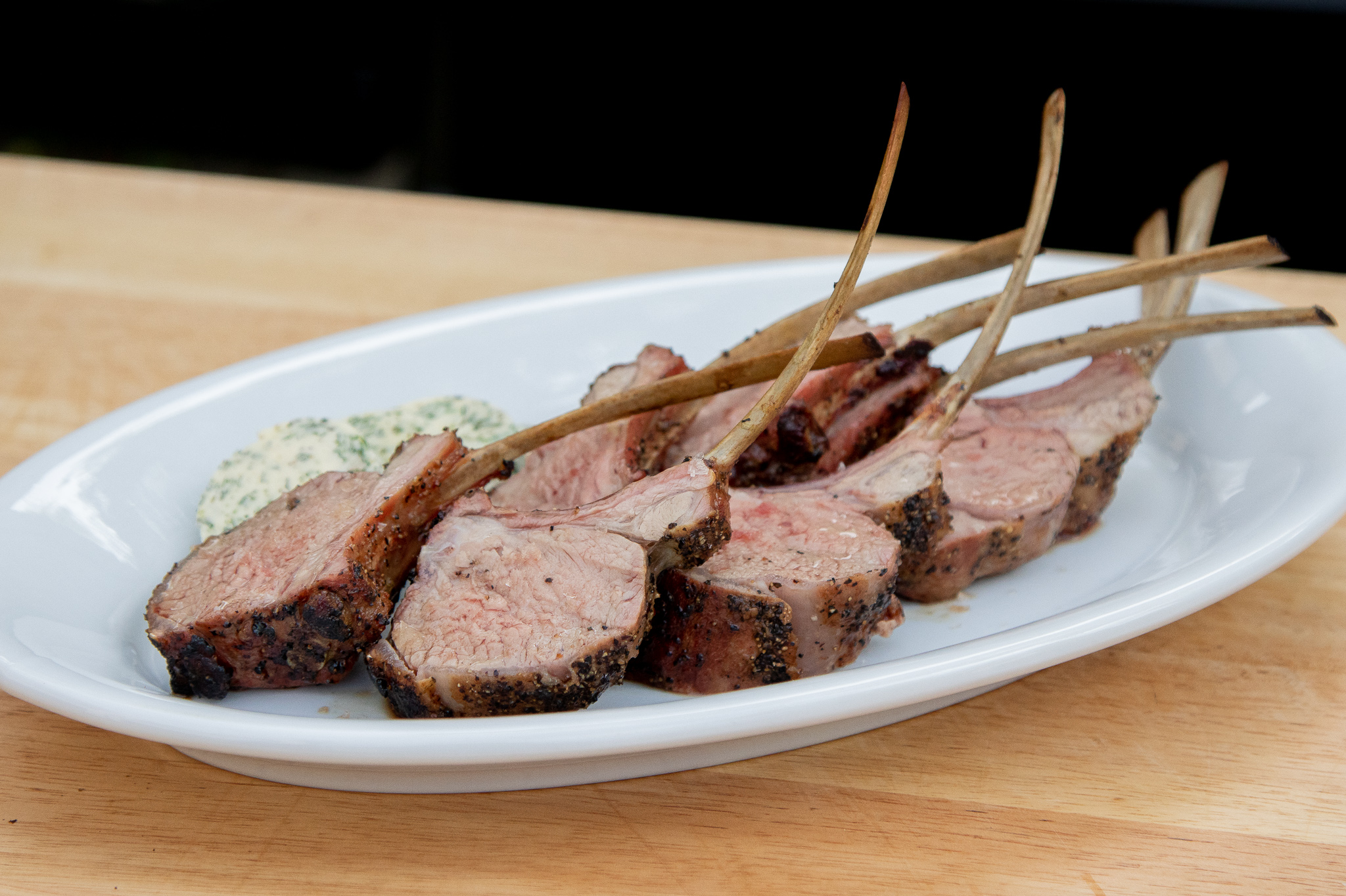 sliced lamb racks on a white plate with a side of mint butter