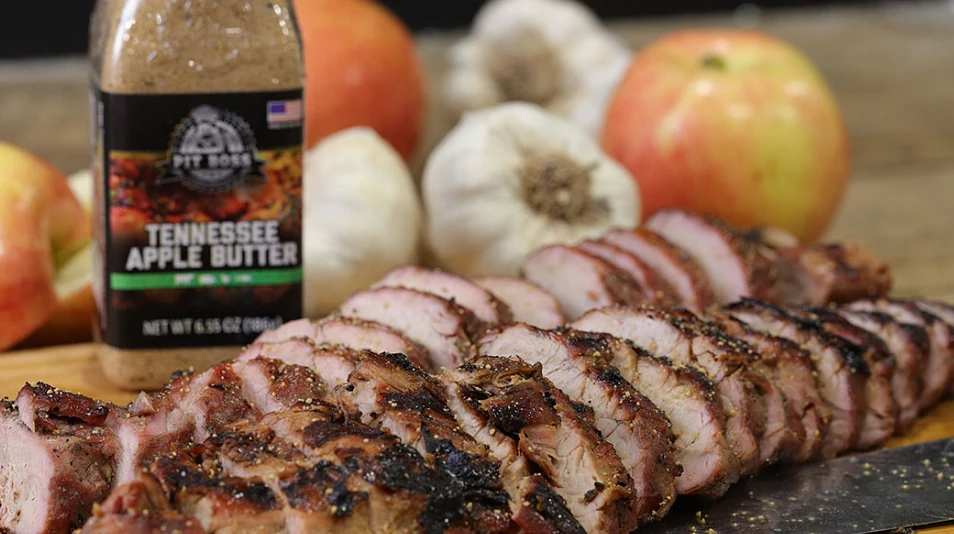delicious looking grilled pork tenderloin sliced and plated next to a bottle of pit boss tennessee apple butter seasoning