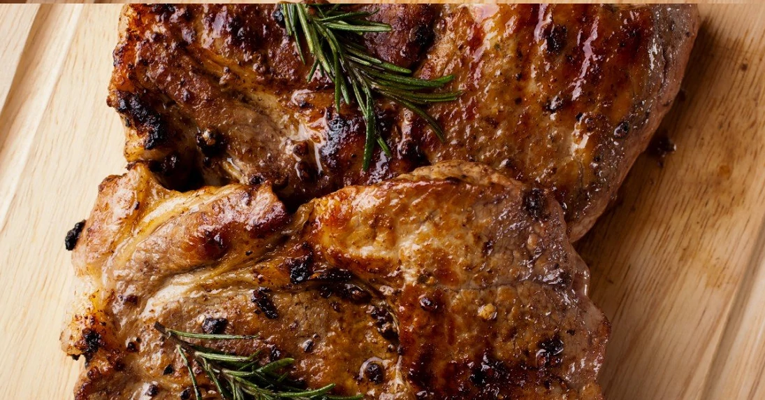 close up of pork chops on wood board with sprigs of rosemary on top