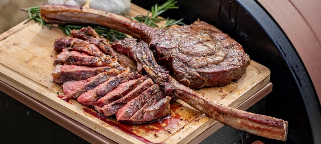 Sliced juicy steak on wooden cutting board next to herbs