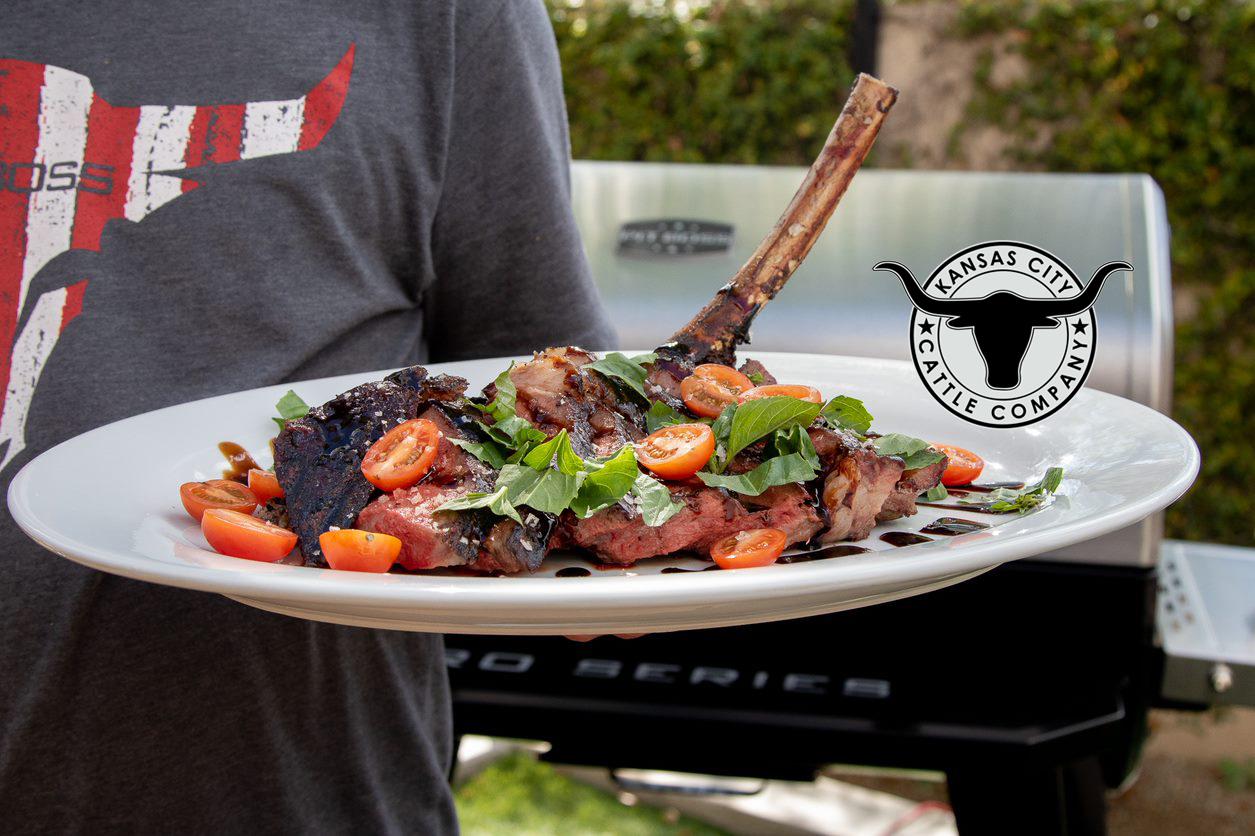 Flame Broiled Grilled Steak garnished with basil, tomatoes, and balsamic on a white plate in front of a Pit Boss Grill