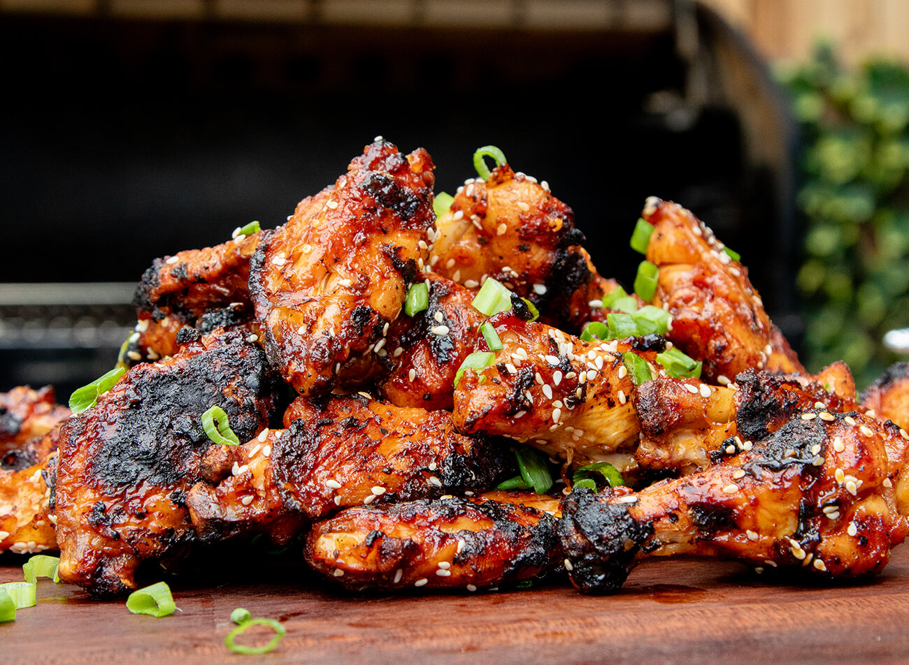 Stacked chicken wings in sauce with sesame seeds and green onion smoked on a pellet grill