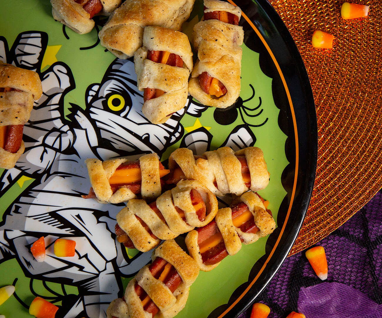 Hot dogs wrapped in dough to mimic the look of a mummy, on Halloween plates