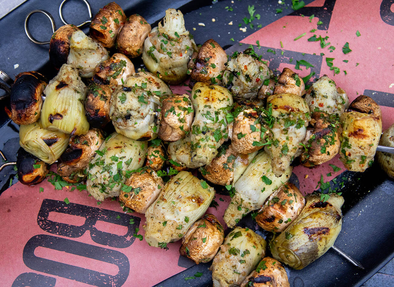 Grilled mushrooms and artichoke hearts on a metal skewer, served on a plate with herb garnish