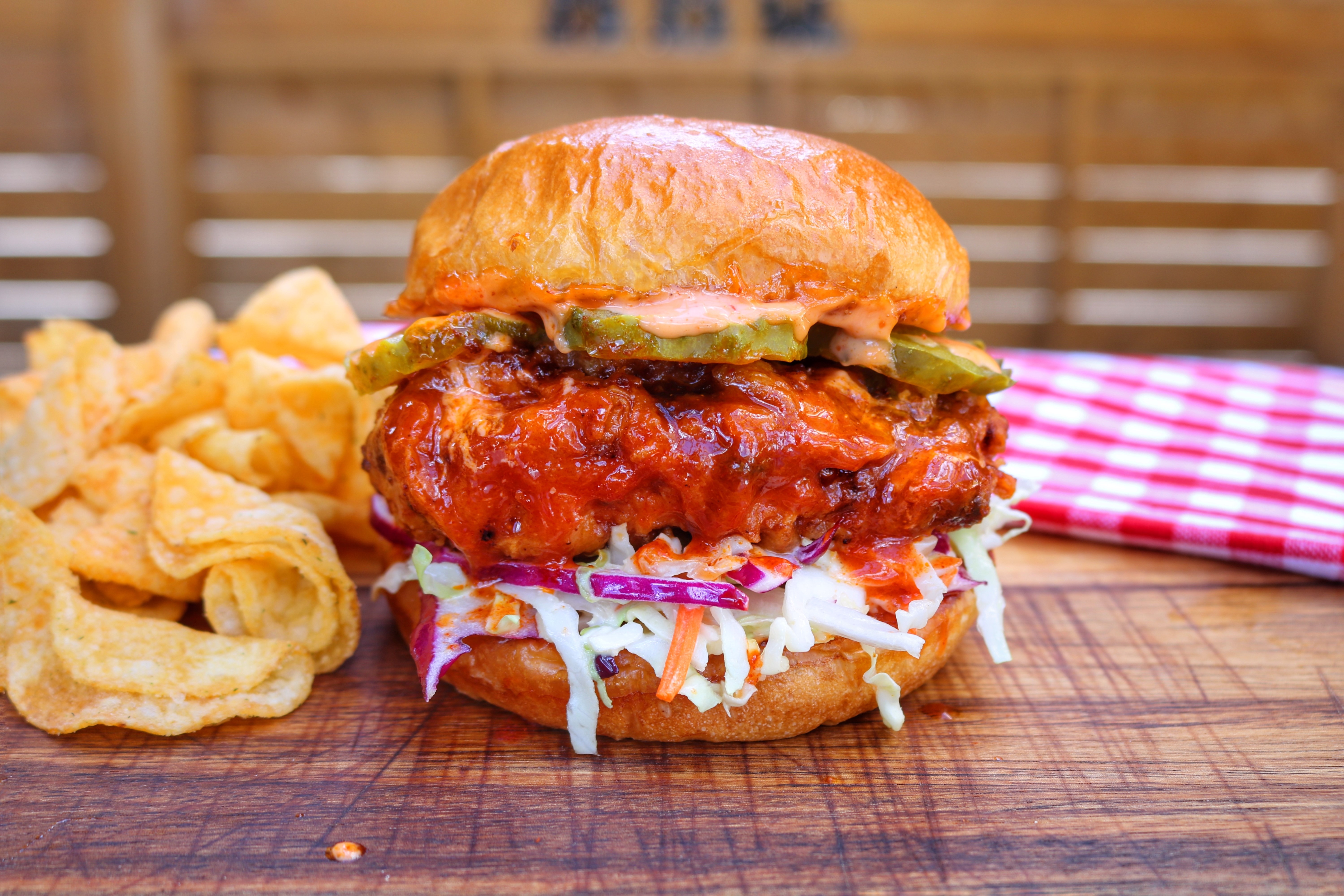 Delicious chicken sandwich with lots of sauce served next to chips on a wooden board