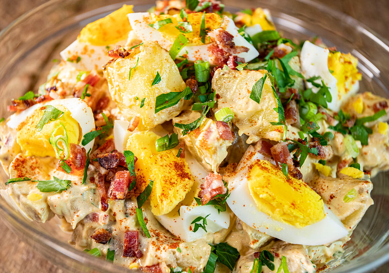 grilled potato salad with smoked hard boiled eggs cooked on a pit boss wood pellet grill served in glass bowl with bacon bits and scallions