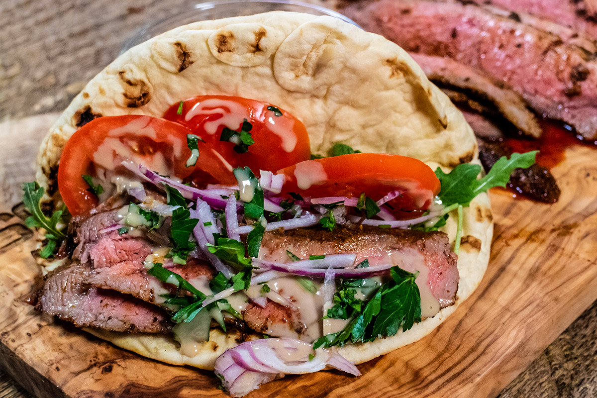 grilled flank steak shawarma pita wraps cooked on pit boss wood pellet grill topped with onions, tomatoes and herbs