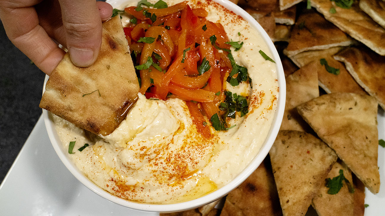 smoked hummus in white bowl with roasted red pepper and grilled pita chips