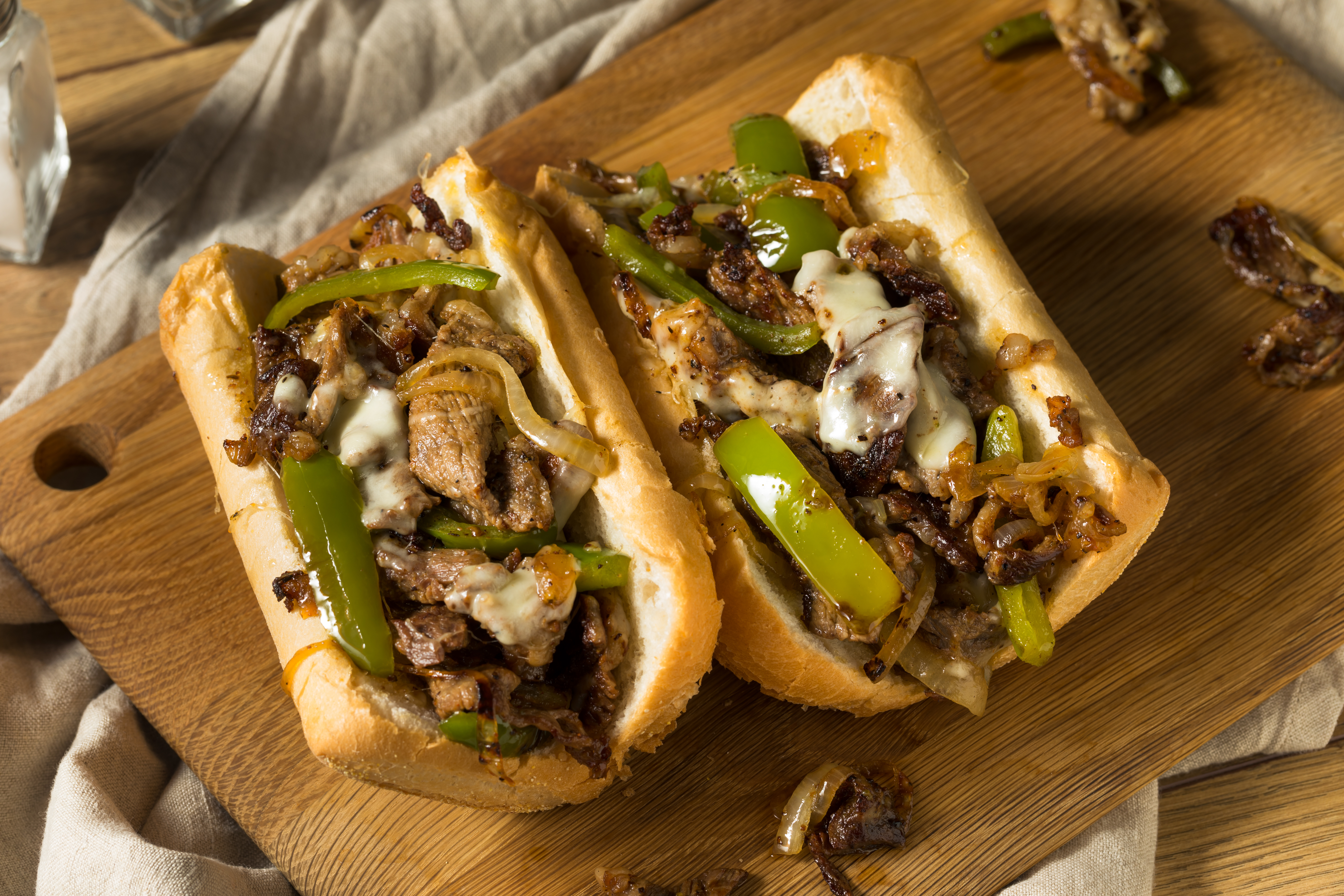 delicious looking Philly Cheese Sandwiches with green peppers on wood cutting board