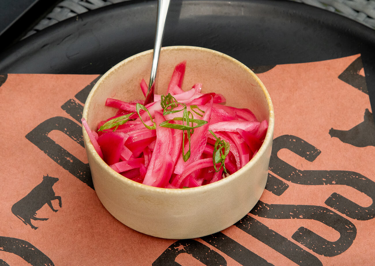 bright pink, pickled red onions, in a bowls with garnish and a spoon