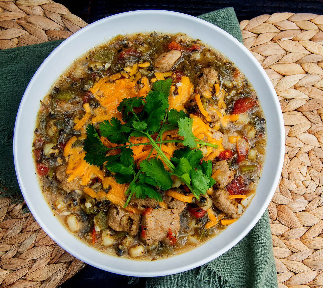 smoked pork green chili cooked on a pit boss wood pellet grill in a cast iron dutch oven served with cheese and cilantro