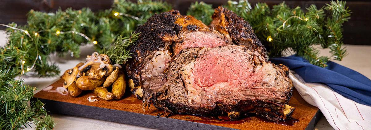 sliced prime rib next to holiday decorations and lights on a wood board