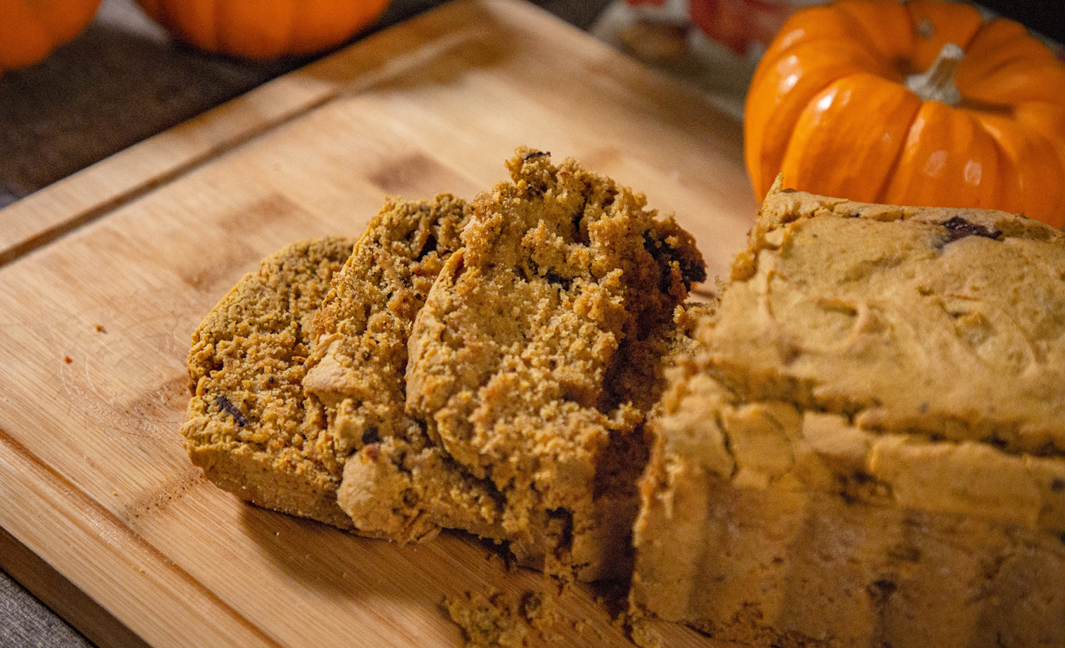 Pumpkin Bread baked on a Pit Boss, sliced on a wooden cutting board with pumpkins and fall leaves