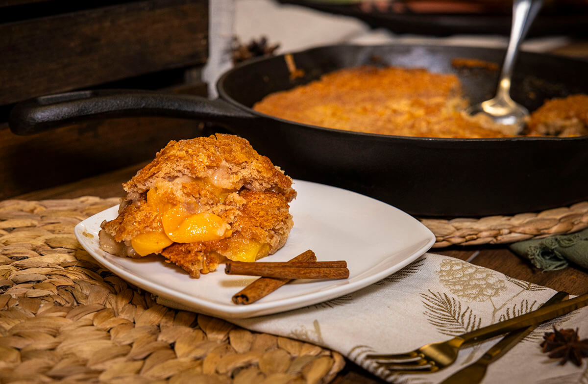 grilled peach cobbler grilled on pit boss grill in a cast iron skillet served on holiday table on plate with cinnamon sticks