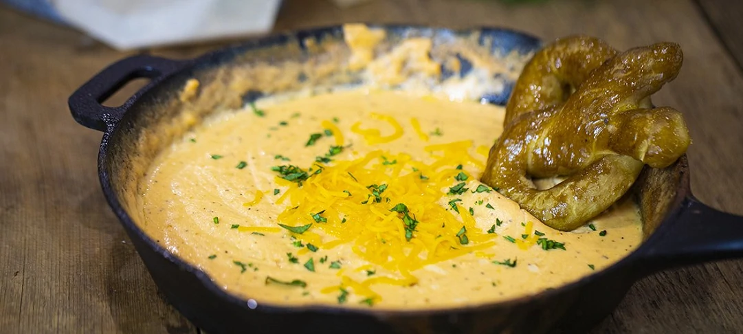 smoked cheesy beer cheese dip in cast iron dish with soft pretzel