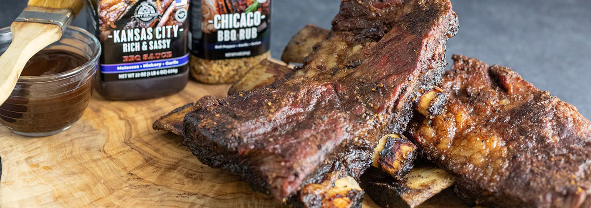 delicious looking Smoked Dino Ribs on wood board with bottles of pit boss kansas city rub and chicago bbq rub