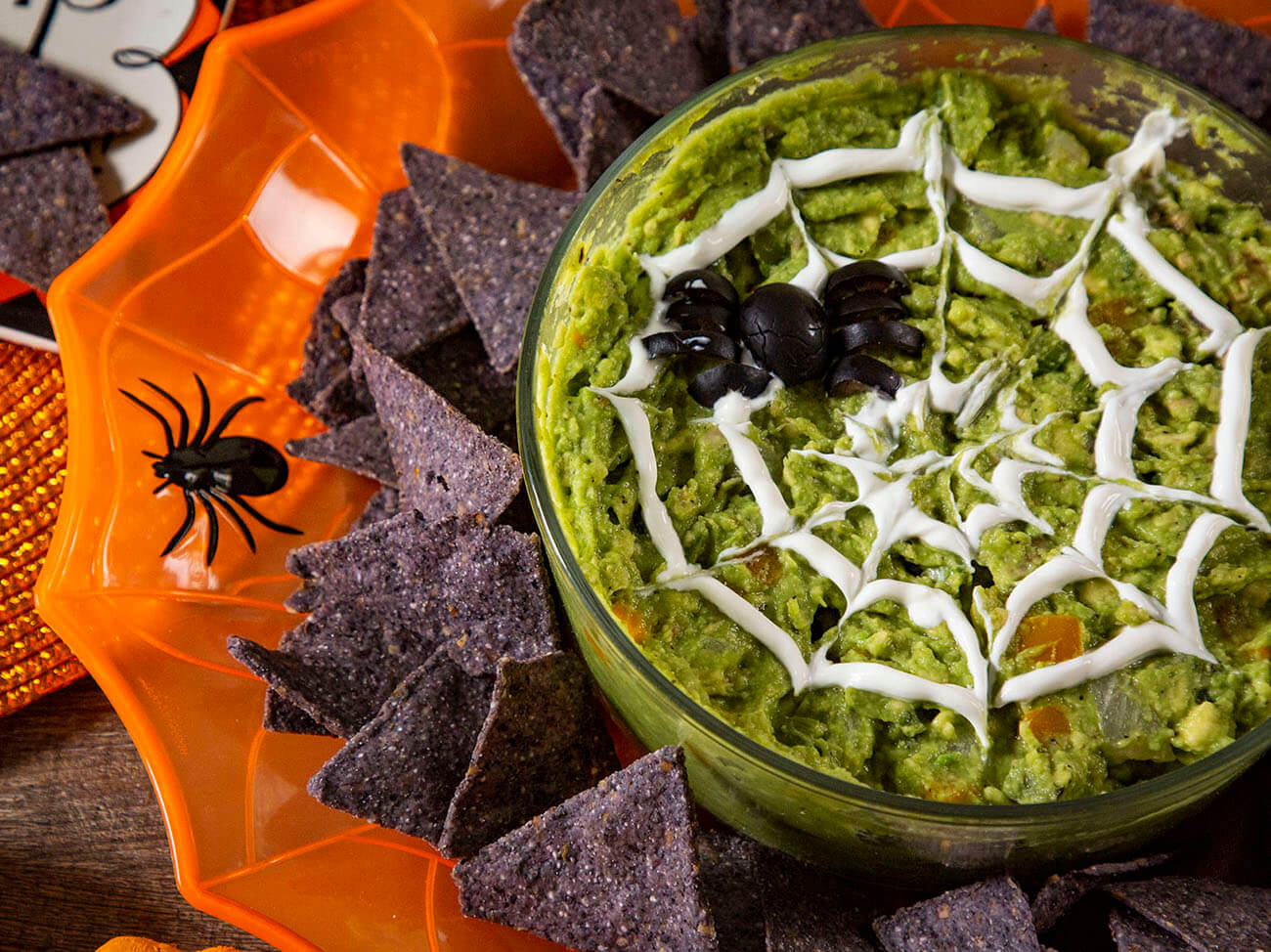 wood pellet smoked Guacamole with sour cream spider webs and black olive spiders on Halloween plates