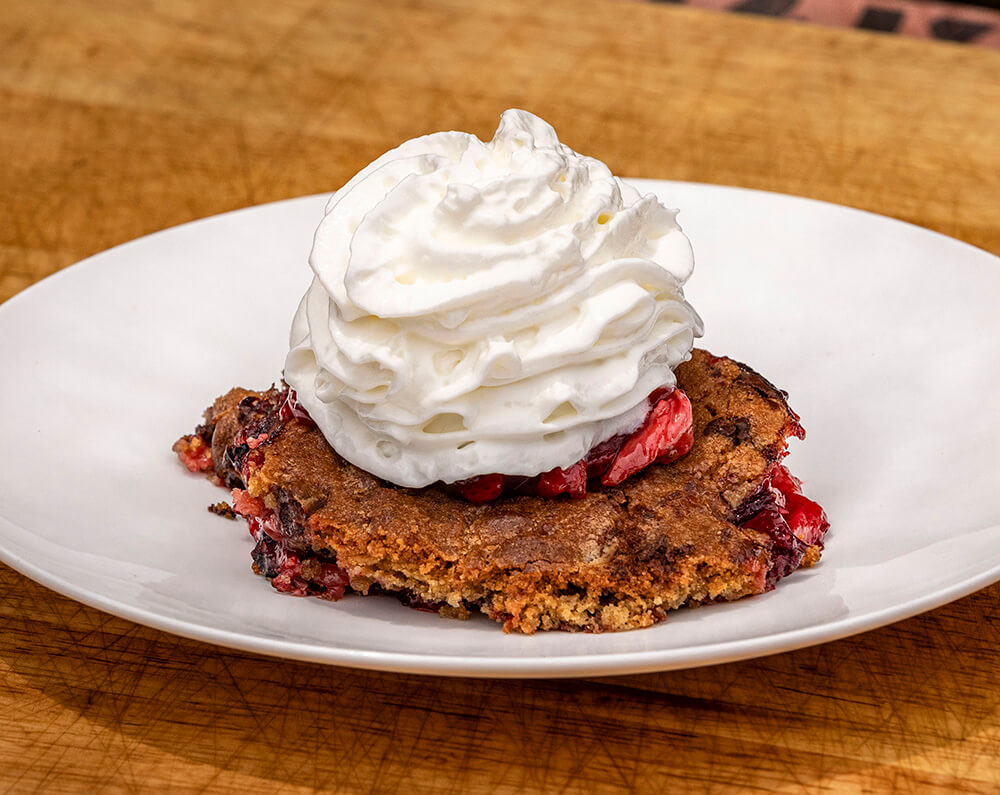 strawberry chocolate chip cookie cobbler cooked on a pit boss wood pellet grill, plated and served with whipped cream