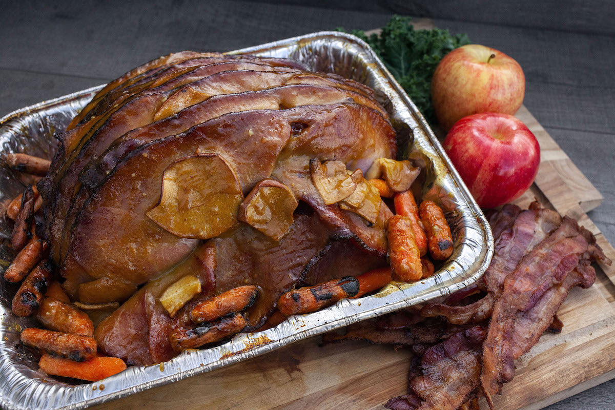 ham with carrots in foil pan next to whole apples and slices of cooked bacon