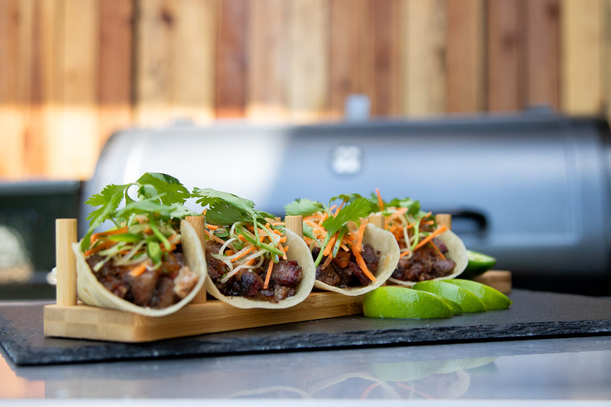 3 crispy beef tacos on a plate in front of pit boss wood pellet smoker