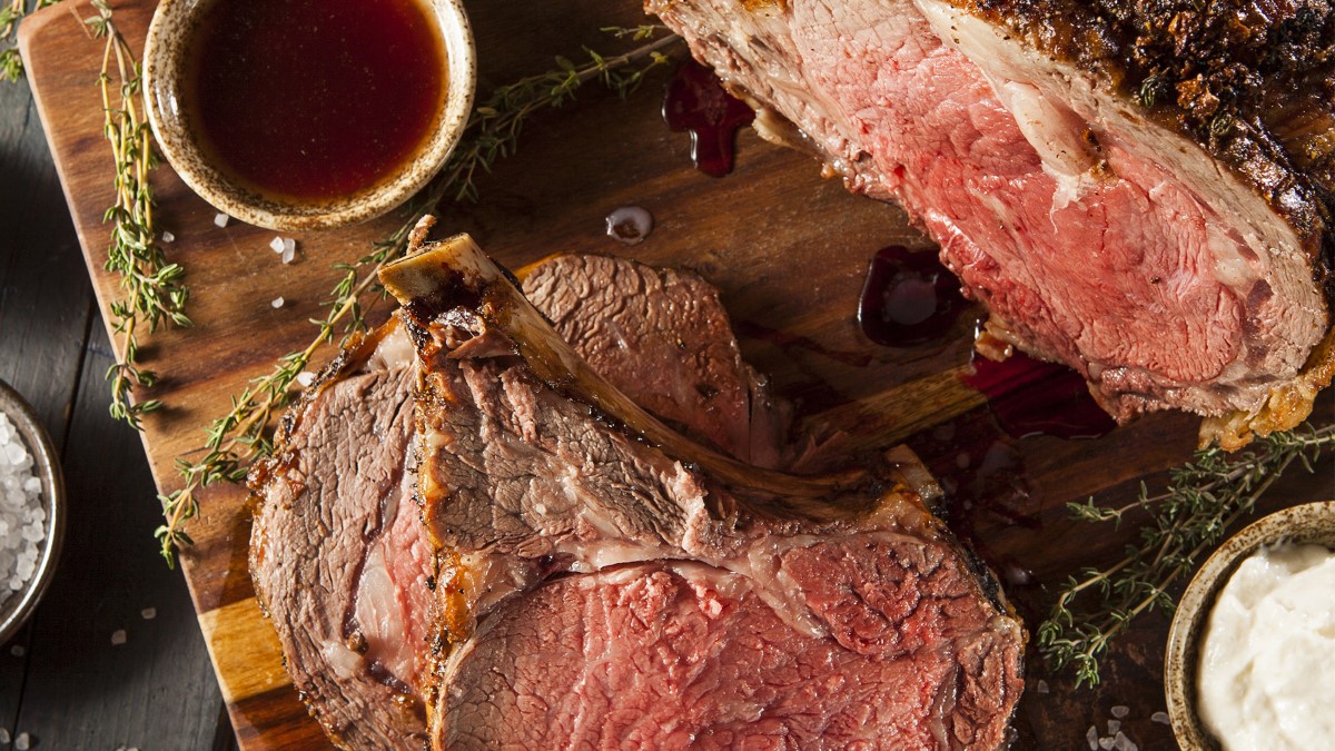 sliced prime rib on wood cutting board with herbs and juices