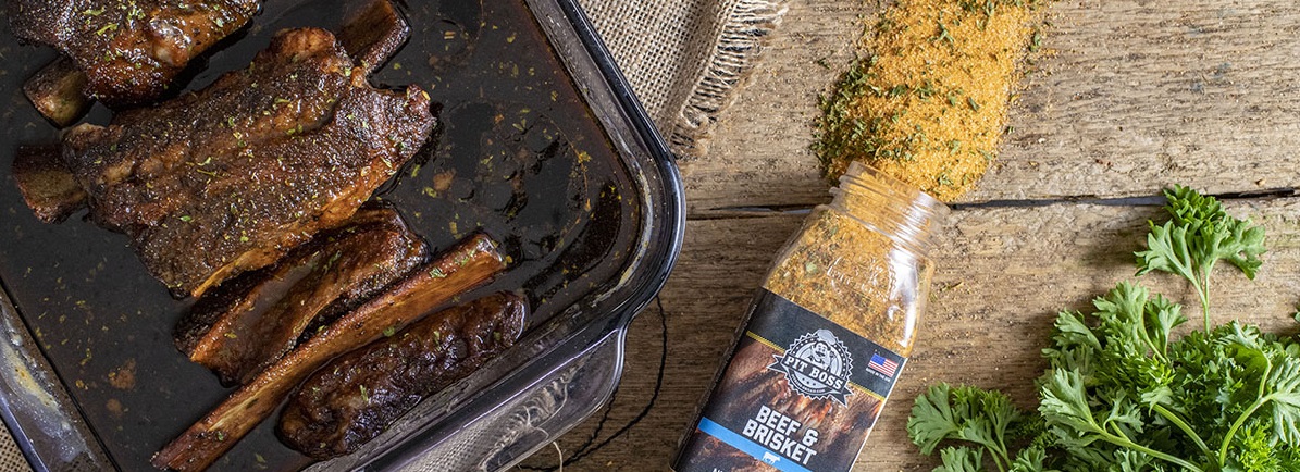 beef short ribs in glass pan with spilled pit boss prime beef rub on wooden table