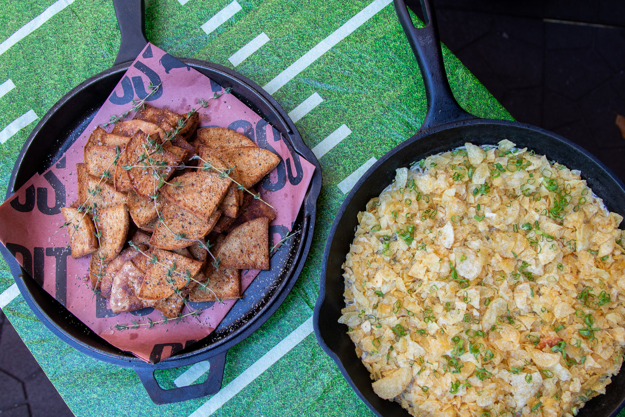 creamy dip with chips in pit boss cast iron with football-themed tablecloth in backgorund