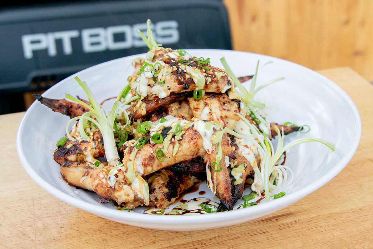 spicy grilled wings grilled on a pit boss wood pellet grill and topped with green onions and chili flakes served in white bowl